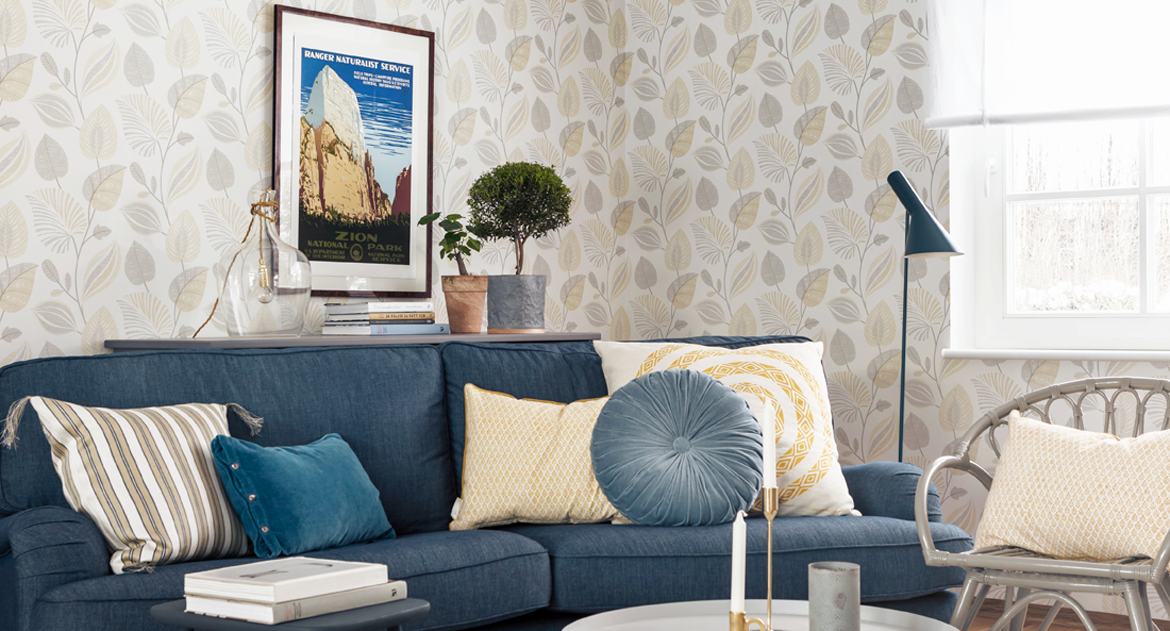 Vardagsrum med blå soffa och kuddar i gult och blått. Tapet med lövmönster. Inspirationsbild.