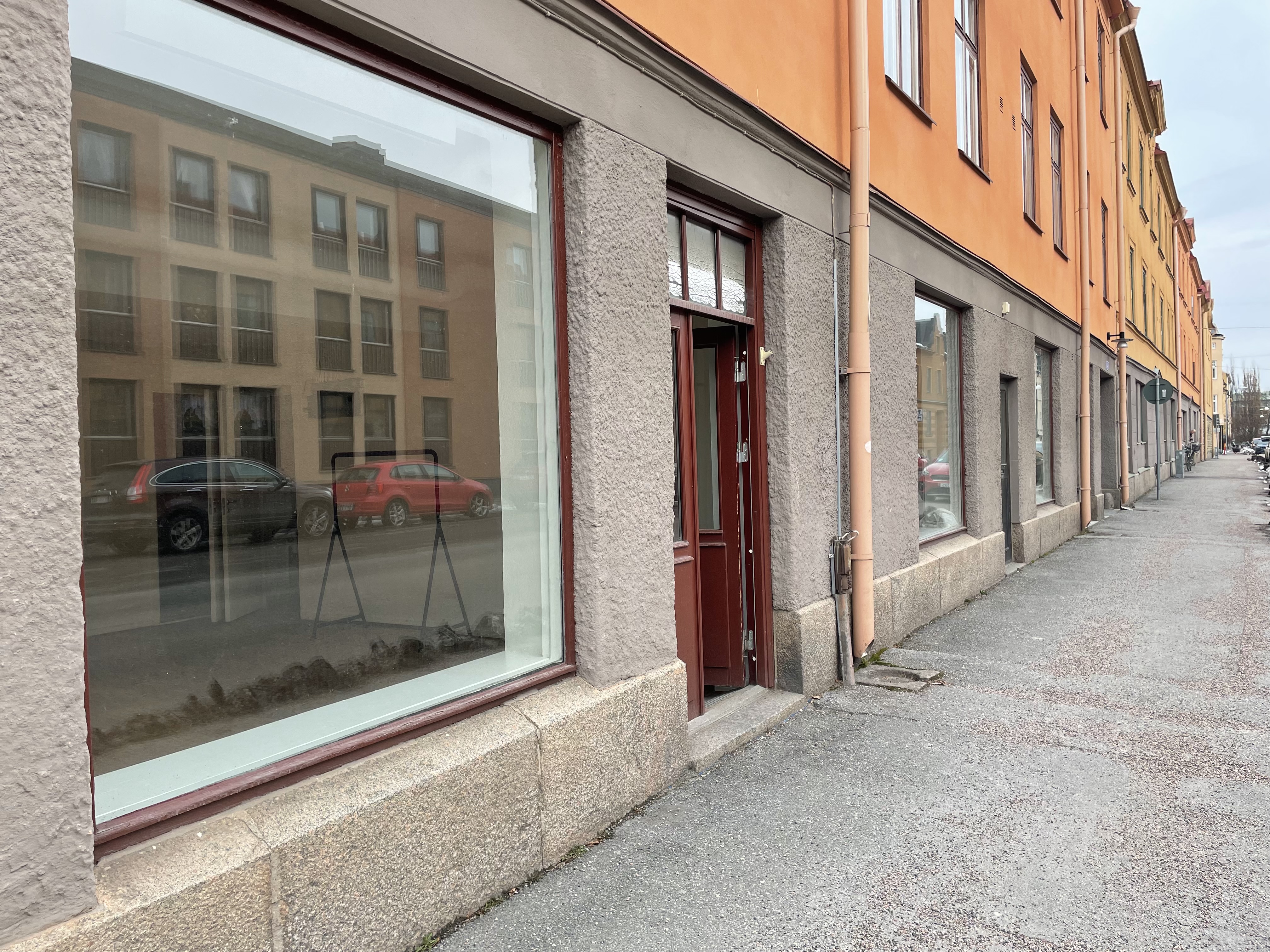 Röd entrédörr och stort skyltfönster till lokal på Karlslundsgatan 8
