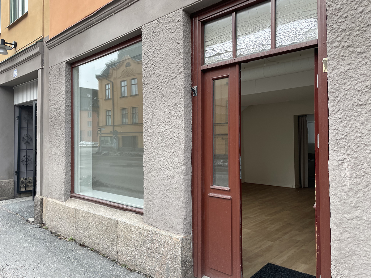 Röd entrédörr och stort skyltfönster på Karlslundsgatan 18.