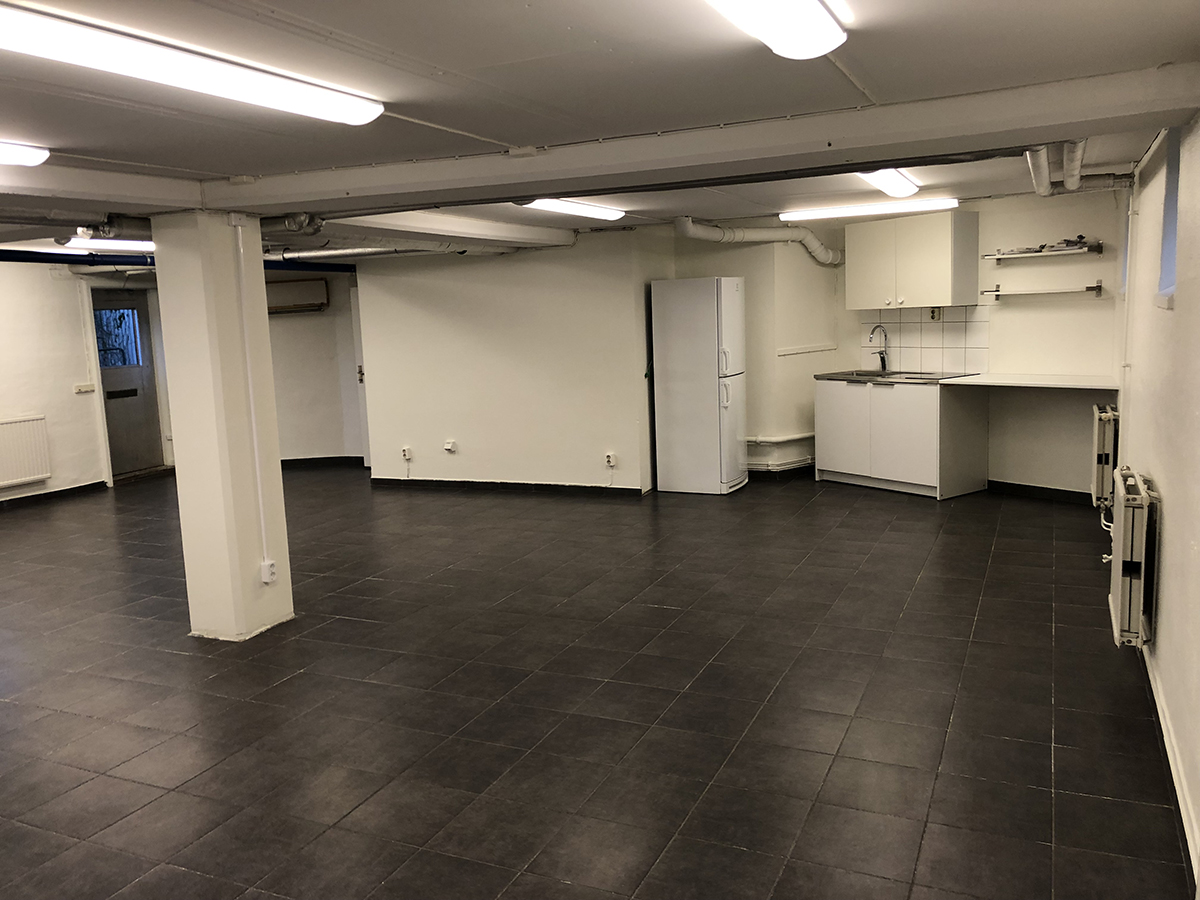 Källarlokal med öppen planlösning, mörkgrått klinkergolv och vita väggar.