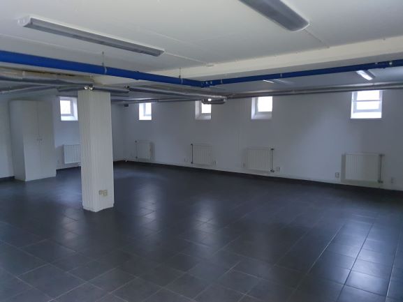 Del i större rum med flera mindre fönster och mörkgrått klinkergolv