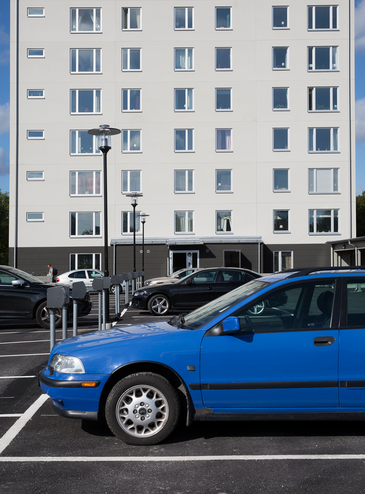 Blå bil står parkerad framför ett höghus.