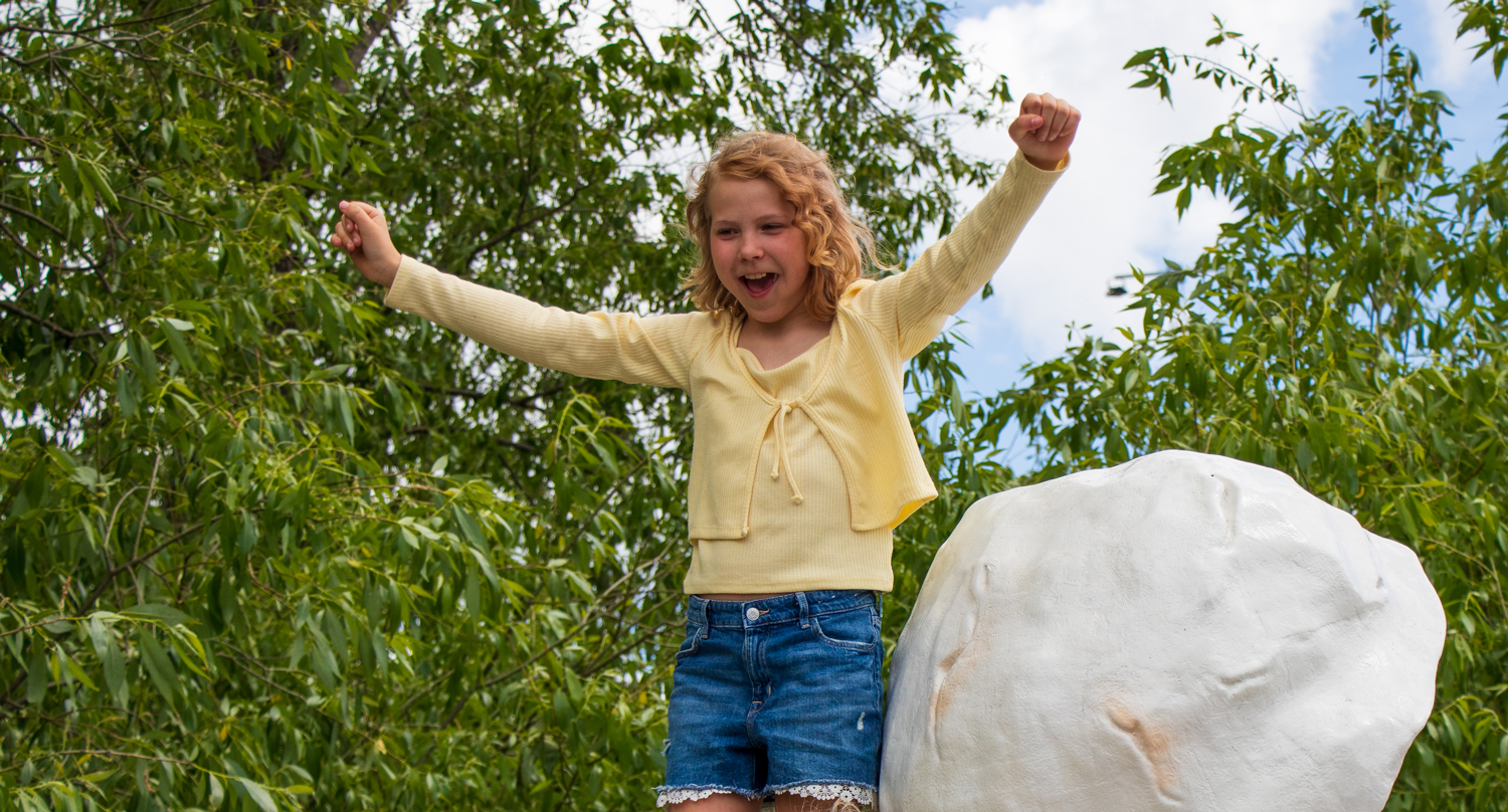 Flicka med gul tröja står uppe på ett av jättepopcornen i Tamarinden. Hon skrattar och håller upp armarna i luften.